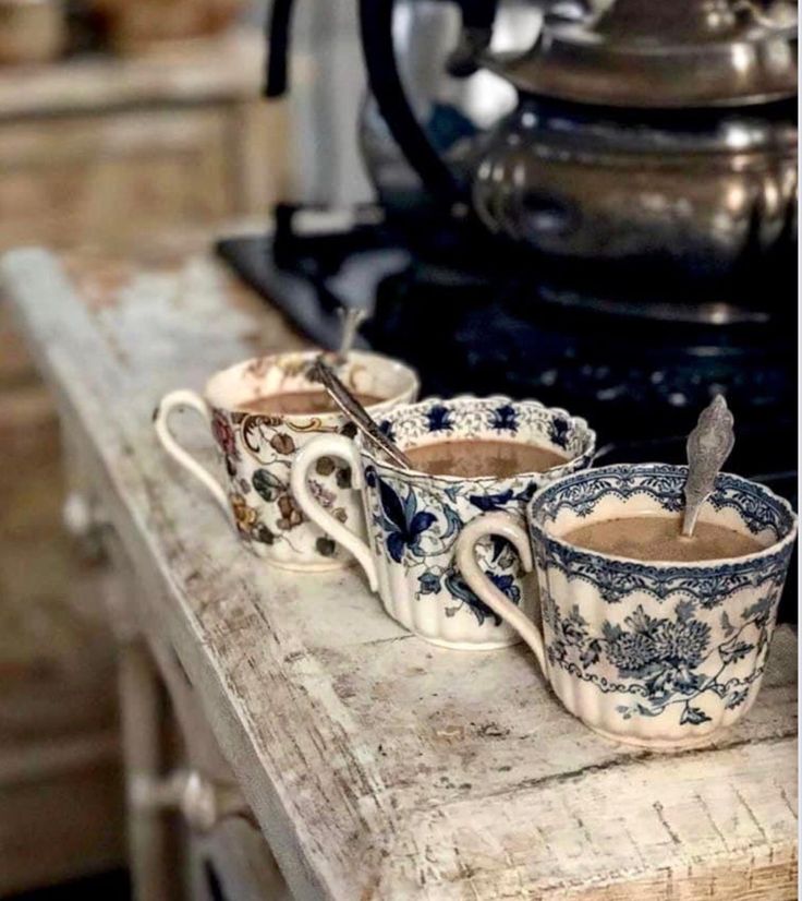 three tea cups sitting on top of a wooden table next to an old fashioned stove