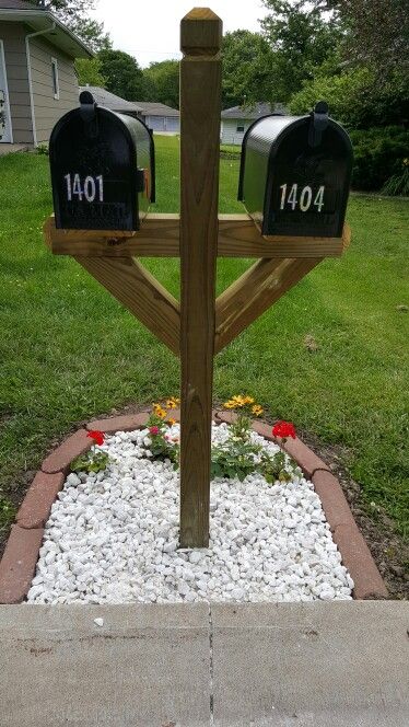 two mailboxes are placed on top of a wooden post in the middle of a flower bed