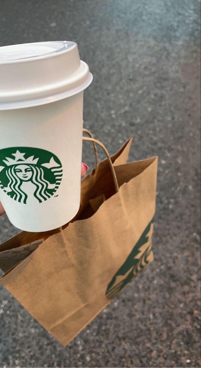 a person holding a starbucks cup and brown paper bag