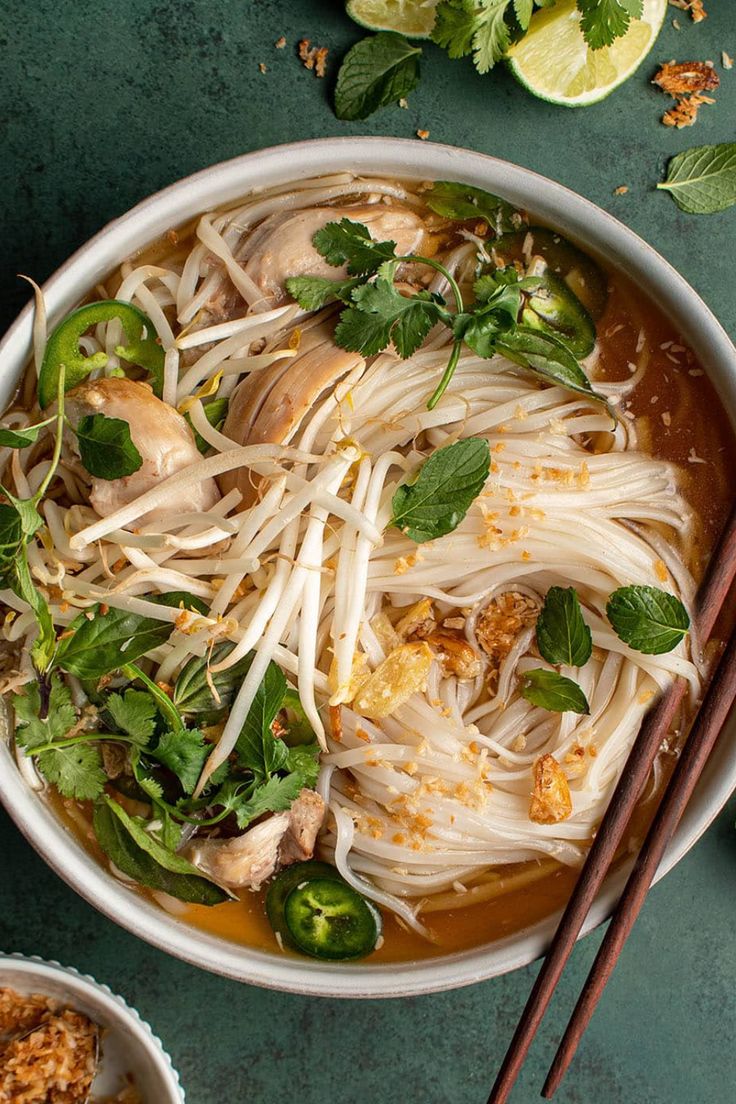 a bowl of noodle soup with chopsticks next to it on a green surface