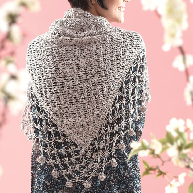 a woman wearing a crocheted shawl with flowers in the back and behind her