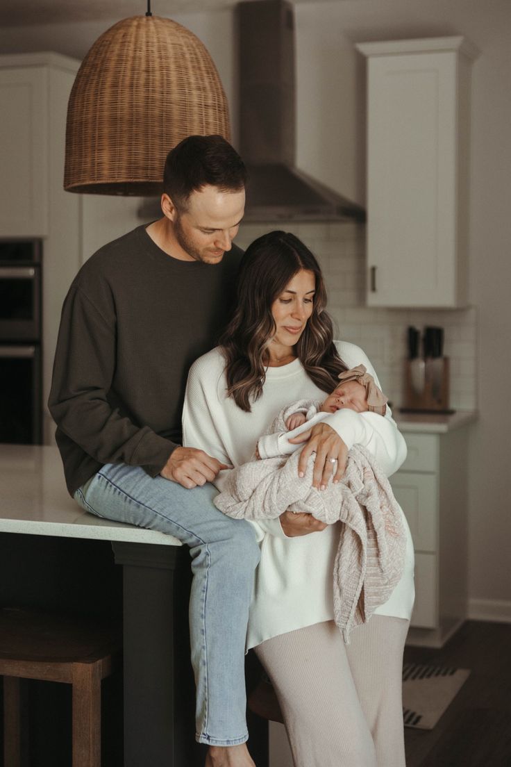 a man and woman holding a baby in their arms while standing next to a kitchen island