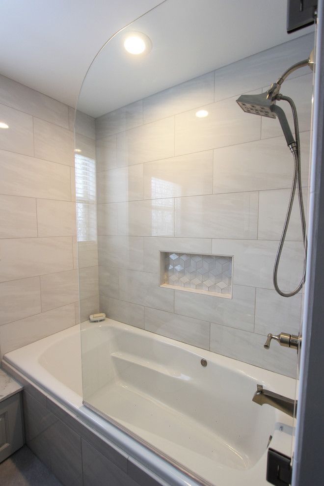 a bath tub sitting next to a toilet under a window in a bathroom with white tiles on the walls