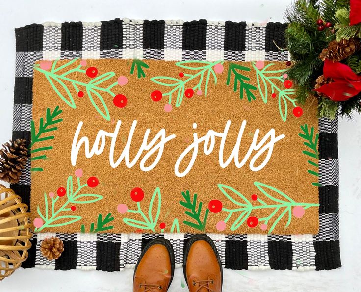 a door mat with the words holly joy written on it next to some pine cones and other holiday decorations