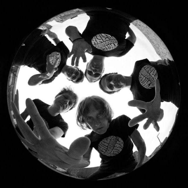 a group of people standing in a circle looking up at the camera with their hands together