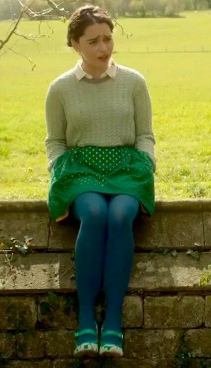 a woman sitting on top of a brick wall next to a green grass covered field