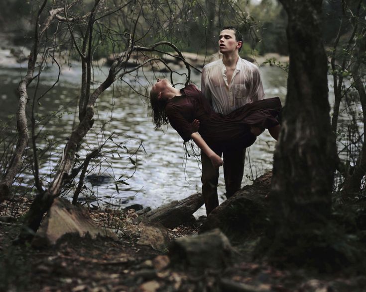 a man is standing on the edge of a river with his arm around a woman's neck