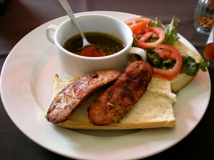 a white plate topped with meat and vegetables next to a bowl of soup on top of bread