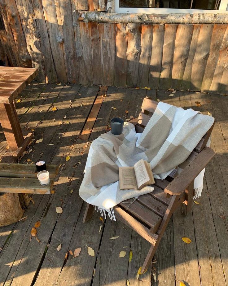 an empty chair on a wooden deck with a blanket draped over it and a cup