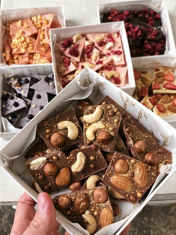 a person holding up a box filled with assorted desserts and nuts in it