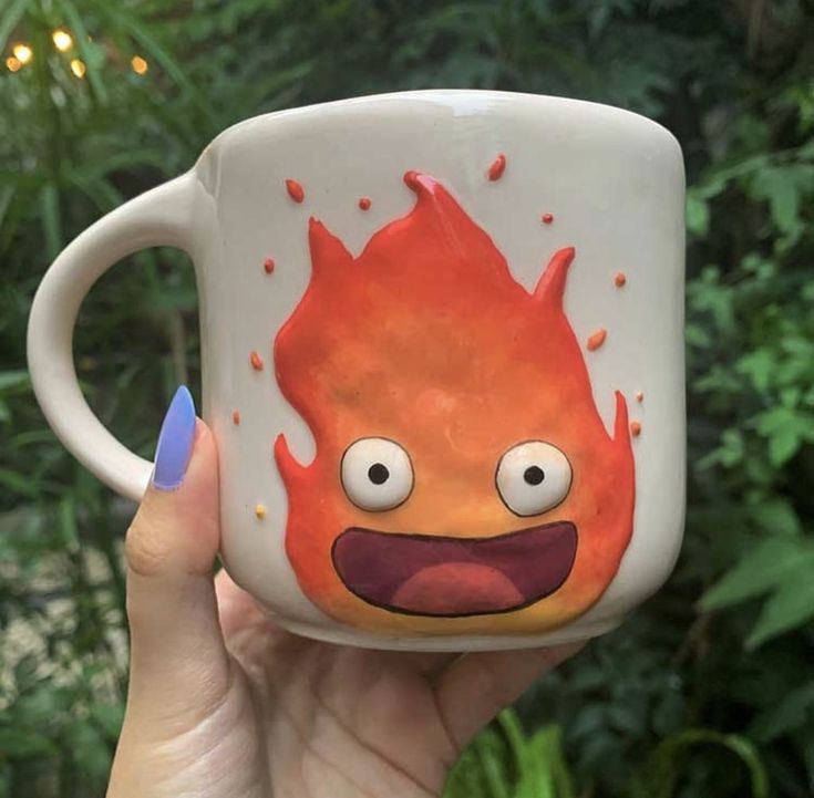 a hand holding a coffee mug with an image of a fireball on it's face