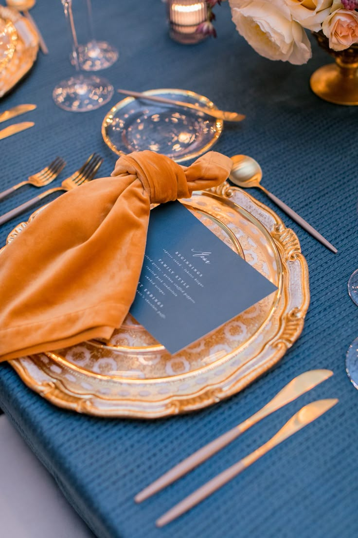 a blue table cloth and gold plates with napkins on it, along with silverware