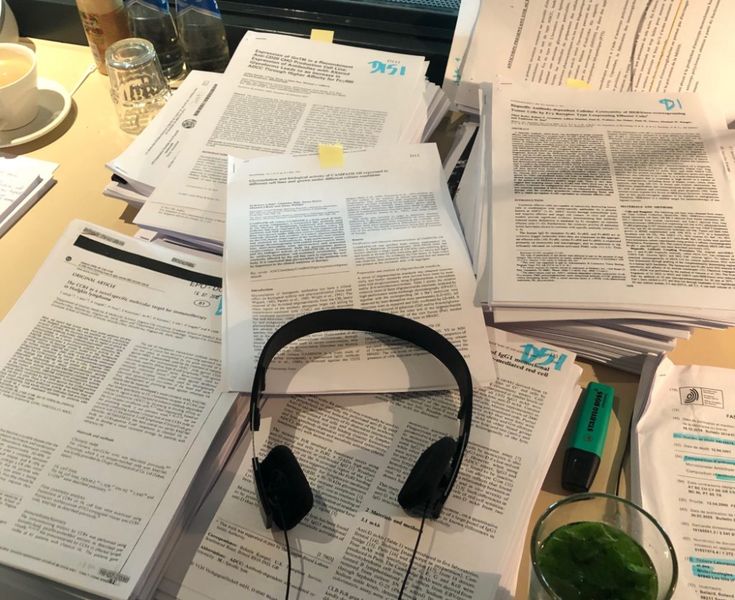 there are many books and headphones on top of the desk with papers all over it