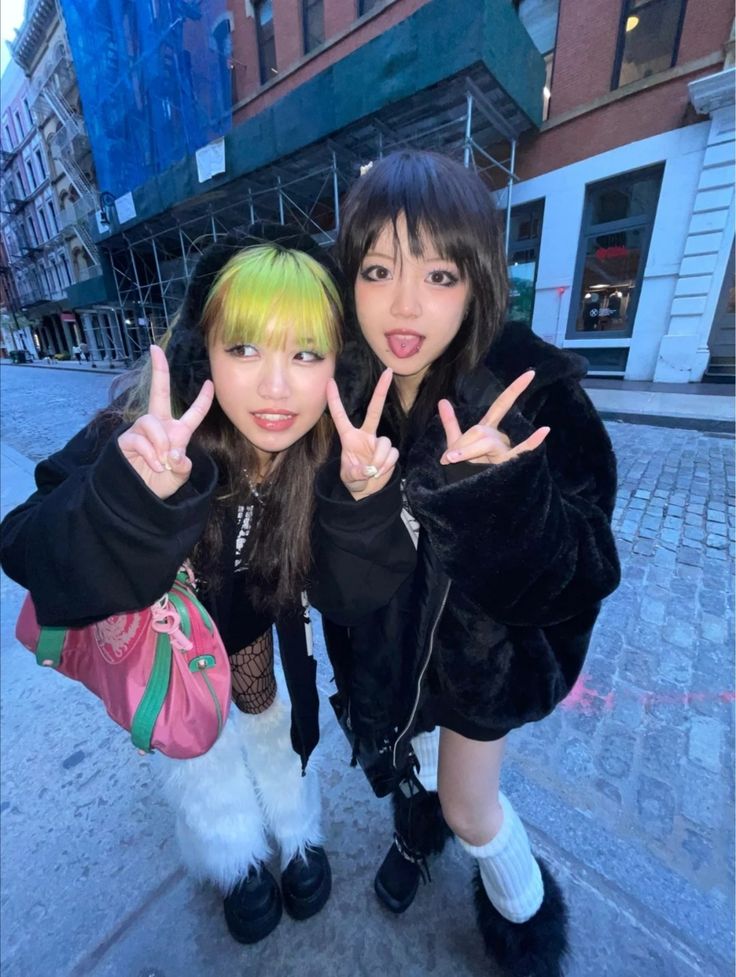 two young women standing next to each other on a sidewalk with their hands in the air