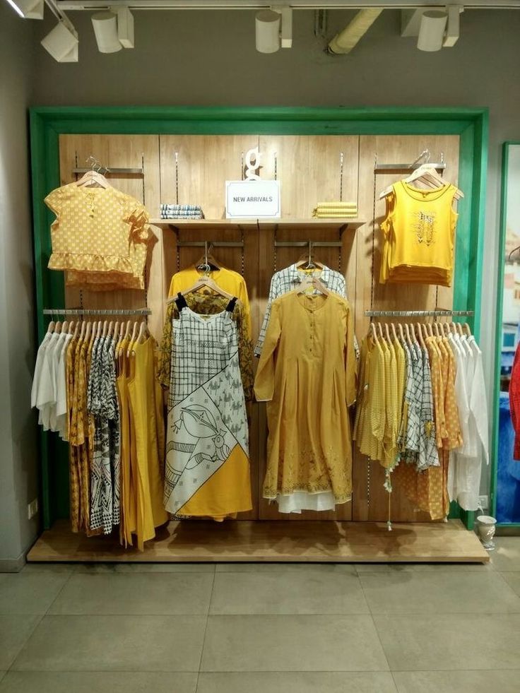 clothes are on display in a store with wooden walls and tile flooring, including yellow shirts