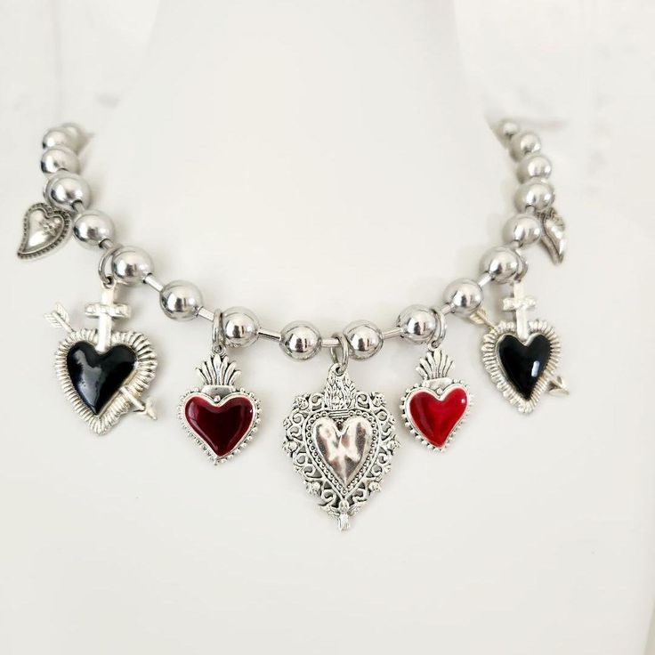 Multi Charms Sacred Heart Necklace - Silver Mexican Miracle Necklace, Ex Voto Bohemian Style, Mexican Jewelry Inspired by Uno de 50, Ideal for Gifting Women at Christmas Product Description: This stunning Multi Charms Heart Necklace is a unique piece of jewelry inspired by the traditional Sacred Heart of Jesus. Featuring a Mexican miracle design and ex voto style, this necklace combines the best of Mexican jewelry with a modern bohemian twist. The silver chain and large hearts make this necklace Bohemian Silver Heart Charm Necklaces, Bohemian Silver Heart Charm Necklace, Bohemian Silver Necklace For Valentine's Day, Silver Bohemian Necklace For Valentine's Day, Valentine's Day Festival Metal Jewelry, Bohemian Jewelry With Heart Beads For Valentine's Day, Bohemian Heart Beads Jewelry For Valentine's Day, Nickel Free Heart Shaped Jewelry For Festivals, Bohemian Silver Heart Necklace