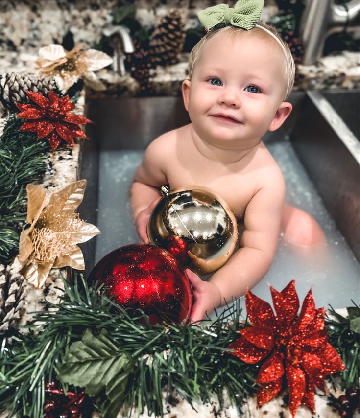 a baby sitting in a sink next to christmas decorations