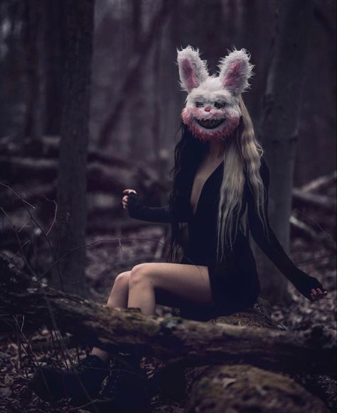 a woman with long hair and bunny ears sitting in the woods wearing an animal mask