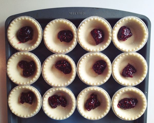 small pies with jam in them sitting on a tray ready to be baked into the oven