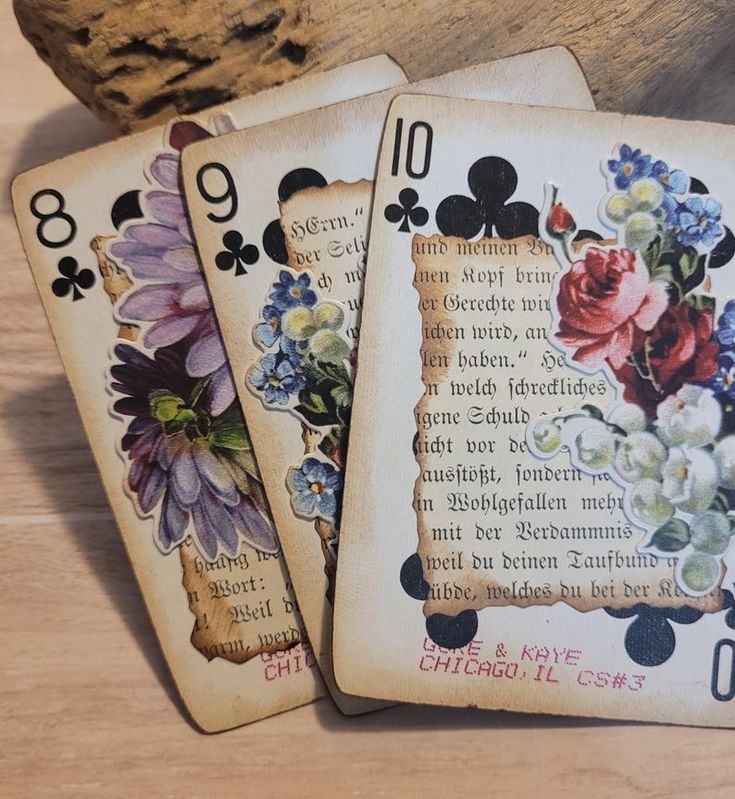 four playing cards with flowers on them sitting next to a rock and some wood planks