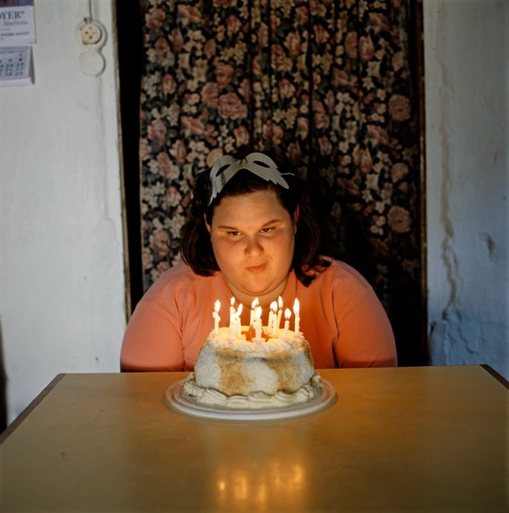 a woman sitting at a table with a birthday cake in front of her and blowing out candles on it