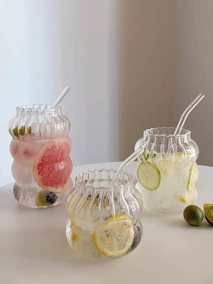 three glass vases filled with different types of drinks and fruit on top of a table