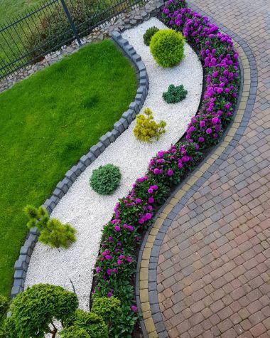 a garden with flowers and rocks in the center, along side a brick path that leads to a fence