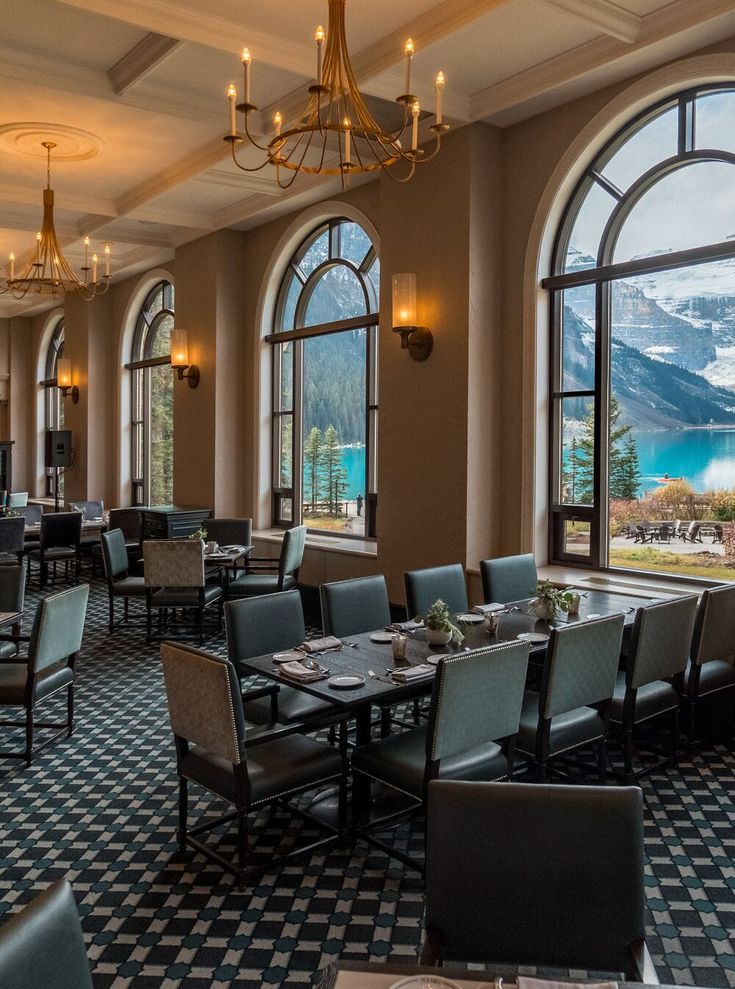 a dining room with tables and chairs near large windows overlooking the lake in front of them