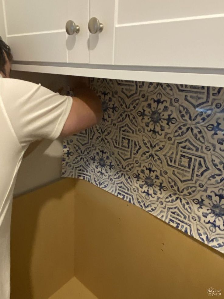 a man is hiding under the counter in his kitchen cupboards with blue and white tiles on it