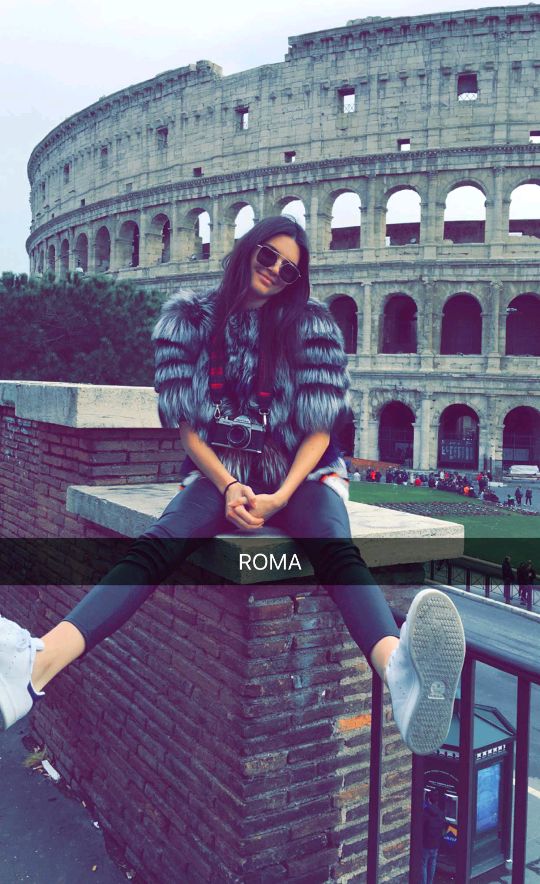 a woman sitting on top of a brick wall in front of an old roman collise