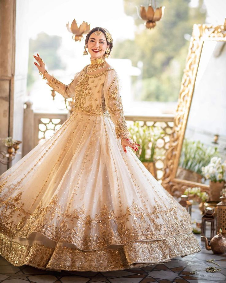 a woman in a white and gold wedding dress standing on a balcony with her arms outstretched