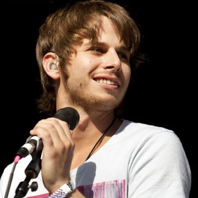 a young man holding a microphone in front of a black background and wearing a white t - shirt