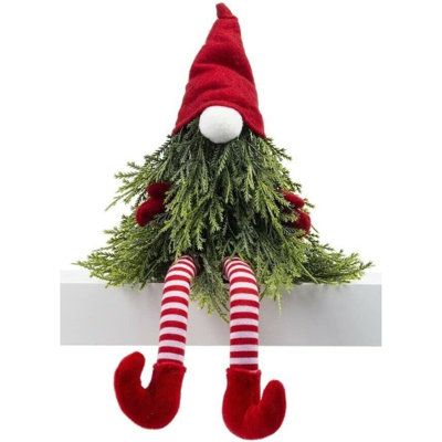 a red and white elf doll sitting on top of a shelf with christmas greenery