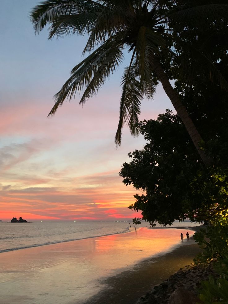 the sun is setting on the beach with palm trees and people walking in the water