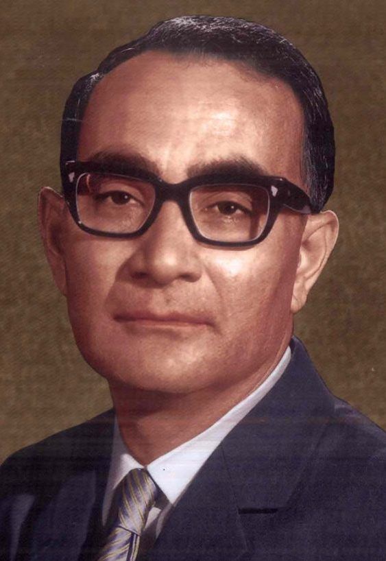 a man wearing glasses and a suit with a tie in front of a brown background