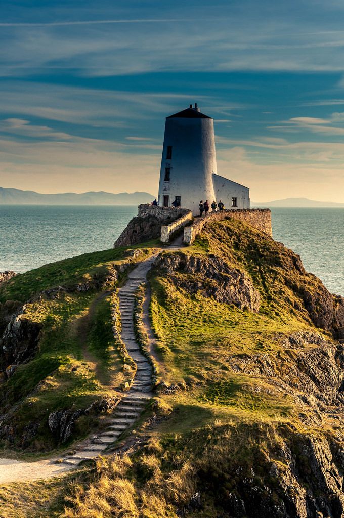 a lighthouse on top of a grassy hill next to the ocean with stairs leading up to it