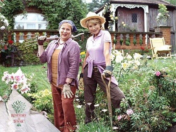 two women are standing in the yard with gardening equipment