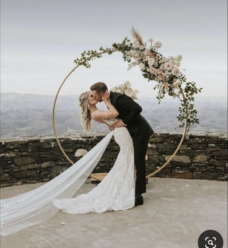 a bride and groom kissing in front of an arch with flowers