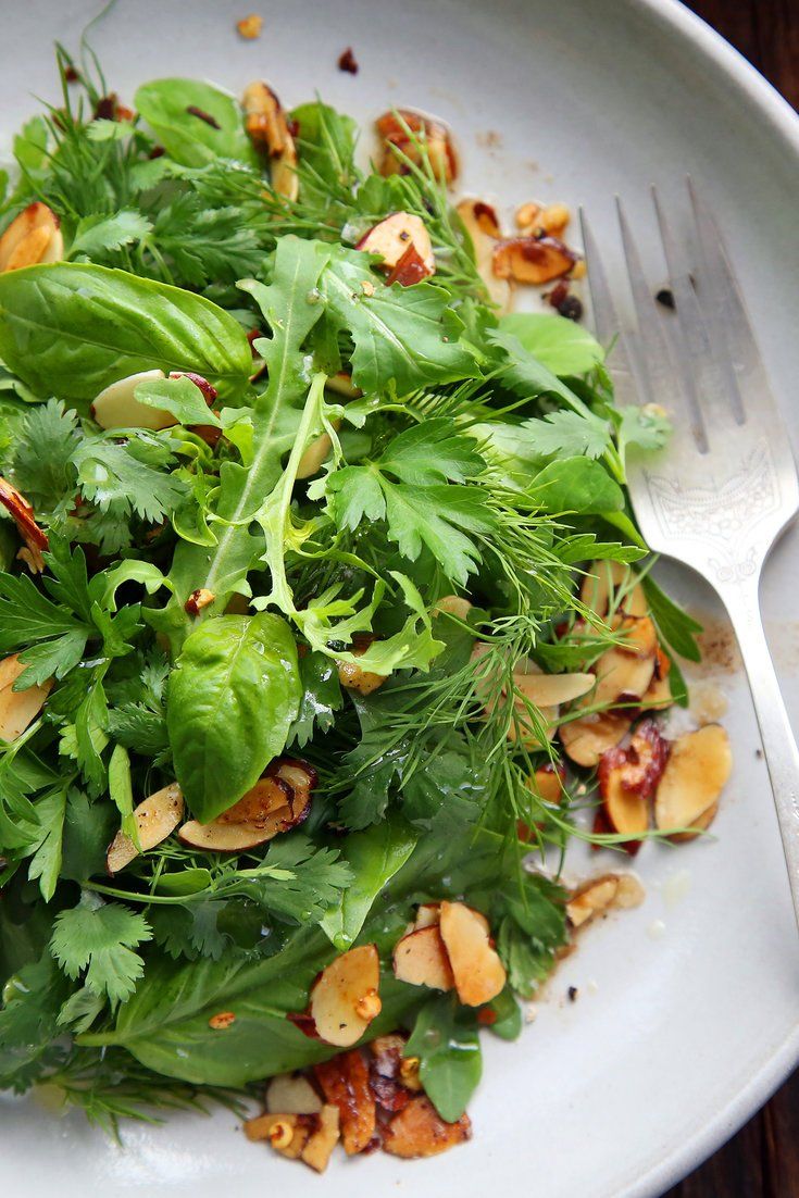 a white plate topped with greens and almonds next to a fork on top of a wooden table