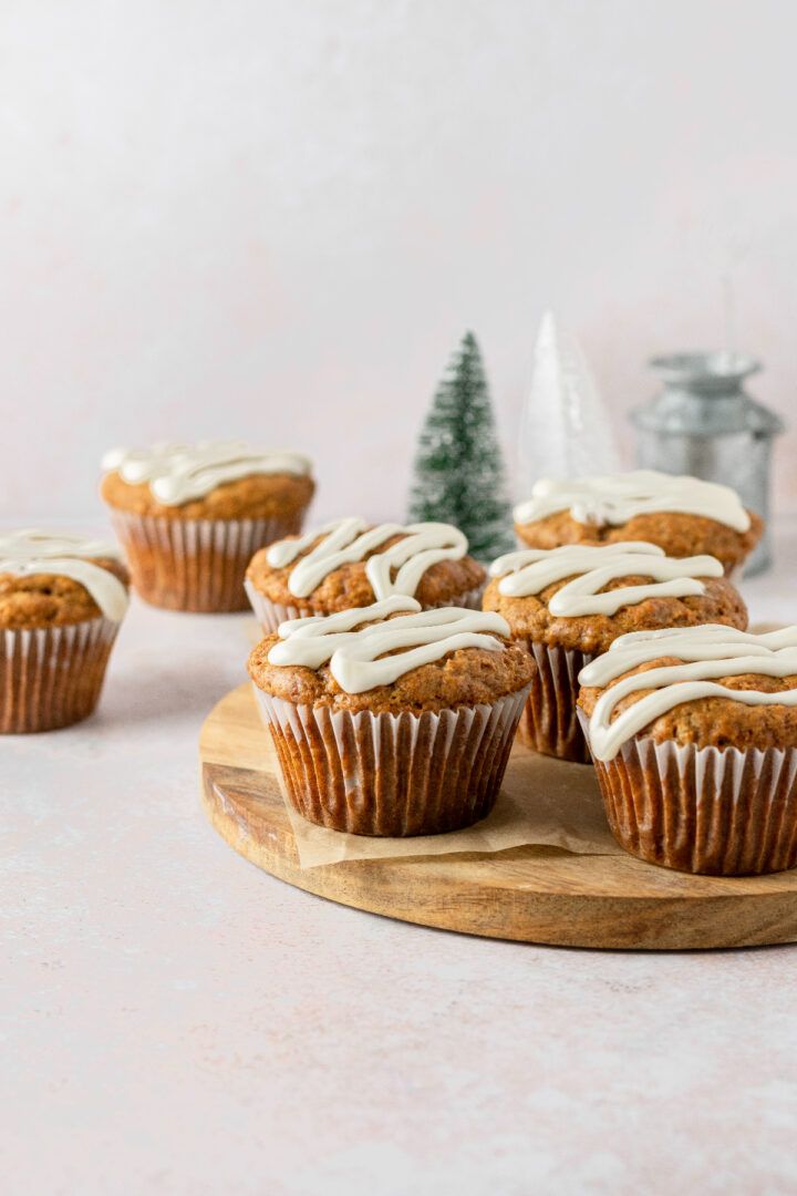 several muffins with icing on a wooden board next to small christmas trees