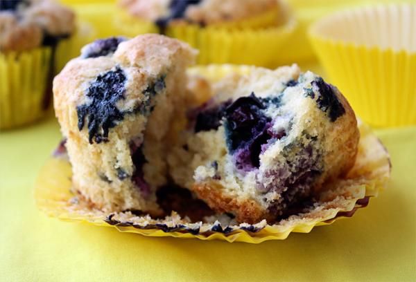 some blueberry muffins are sitting on a yellow tablecloth with other muffins in the background