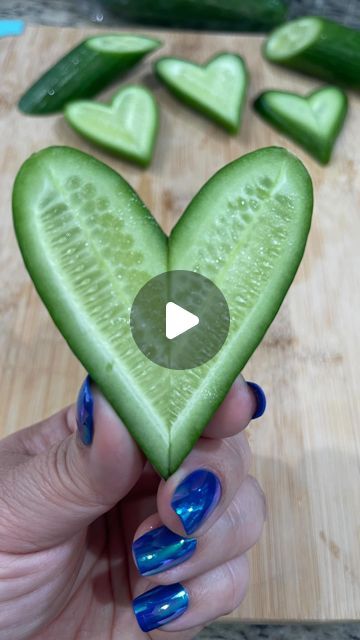 a person holding up a cucumber shaped like a heart with blue nail polish