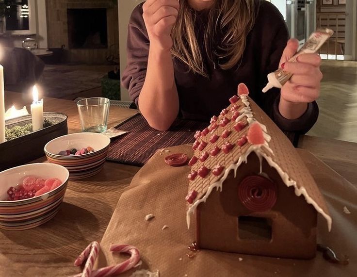 a woman sitting at a table in front of a gingerbread house with candles on it