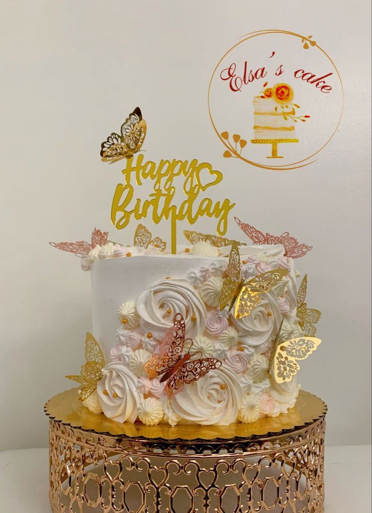 a birthday cake with white frosting and gold butterflies on top is sitting on a golden stand