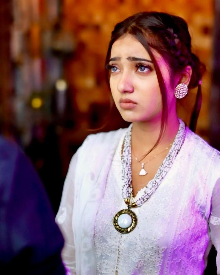 a young woman in a white dress with necklaces and earrings on her neck looking at the camera