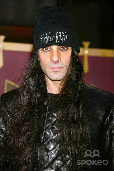 a man with long hair wearing a black hat and leather jacket, looking at the camera