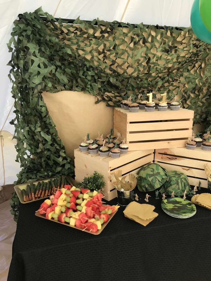 a table topped with lots of food next to a wall covered in greenery and balloons