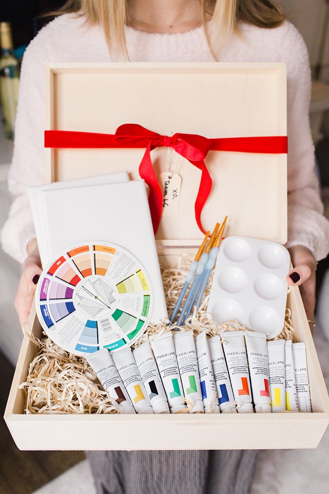 a woman holding a box filled with paint and supplies for her painting project in it