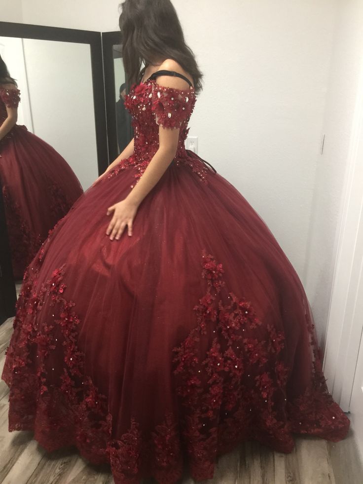 a woman in a red ball gown looking at herself in the mirror with her hand on her hip