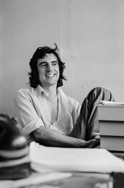 a black and white photo of a man sitting at a desk with his legs crossed